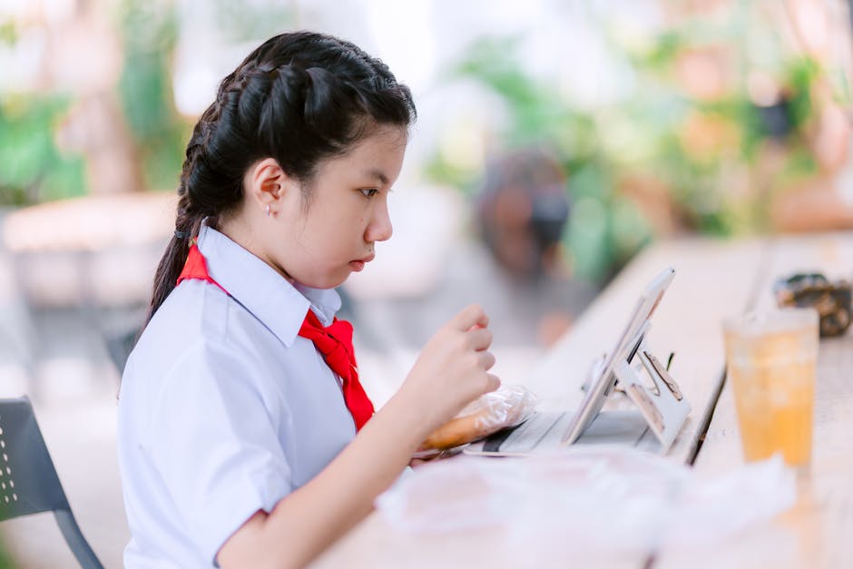 制服を着た集中した学生が屋外のカフェでタブレットを使い、デジタル学習をしています。